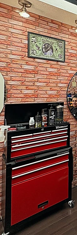 Cajonera roja de herramienta con productos de barbería encima, junto al muro de ladrillo