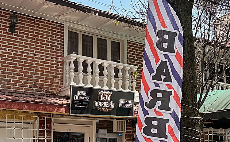 Fachada de ladrillo con balcón blanco y la bandera roja, azul y blanca que dice Barber