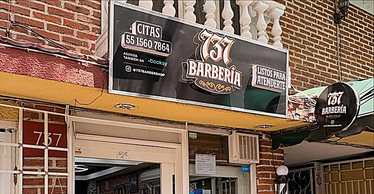 Fachada de ladrillo con el letrero negro de 737 Barbería, el número 737 pintado junto a la puerta y el poste de barbero