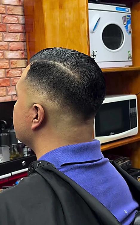Corte de espaldas con raya marcada, fade y cabello peinado hacia atrás